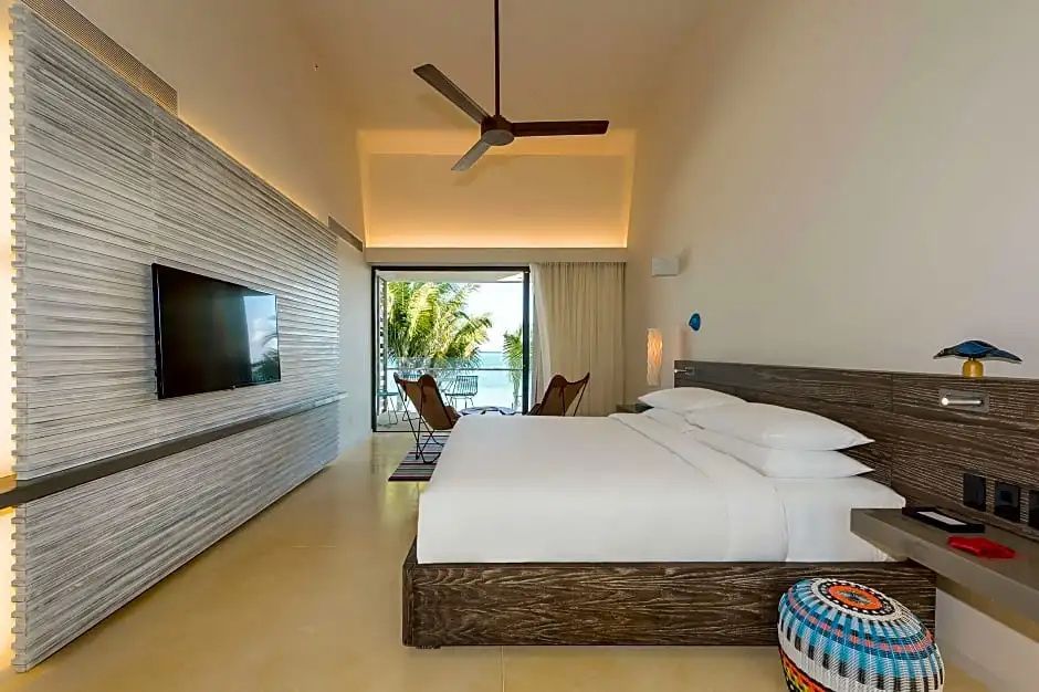 Zimmer mit großem Bett, Deckenventilator und Schiebetür zur Terrasse am Meer.