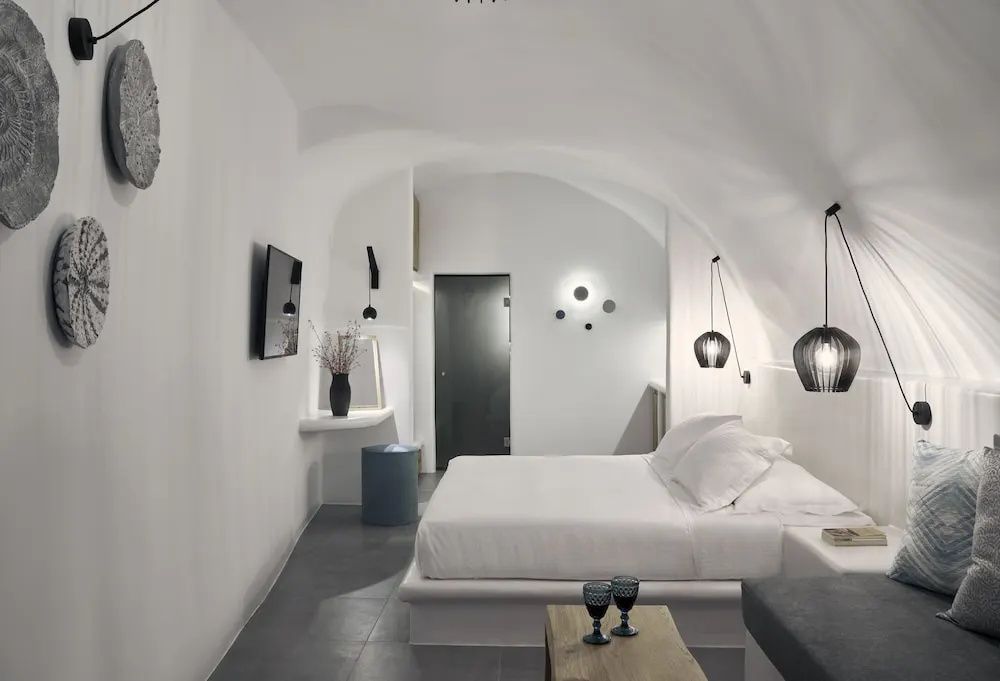 Weißes Höhlenschlafzimmer mit Doppelbett, gewölbter Decke und moderner Beleuchtung.