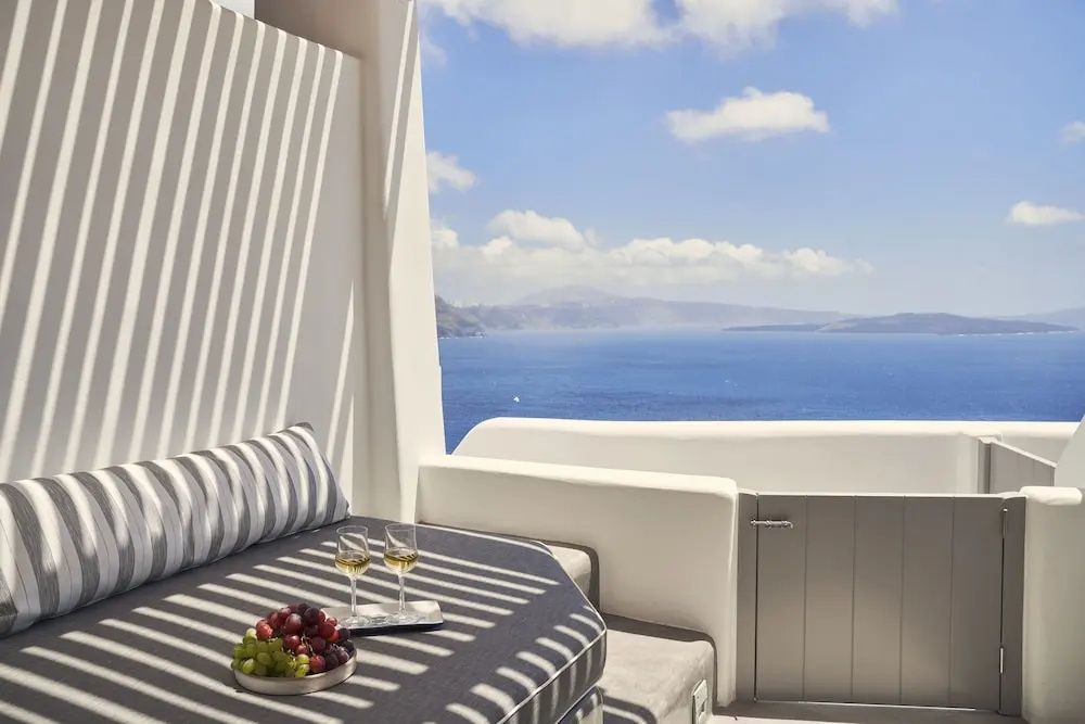 Sonnige Terrasse mit gepolsterter Liege, Obstschale und Blick auf das blaue Meer.