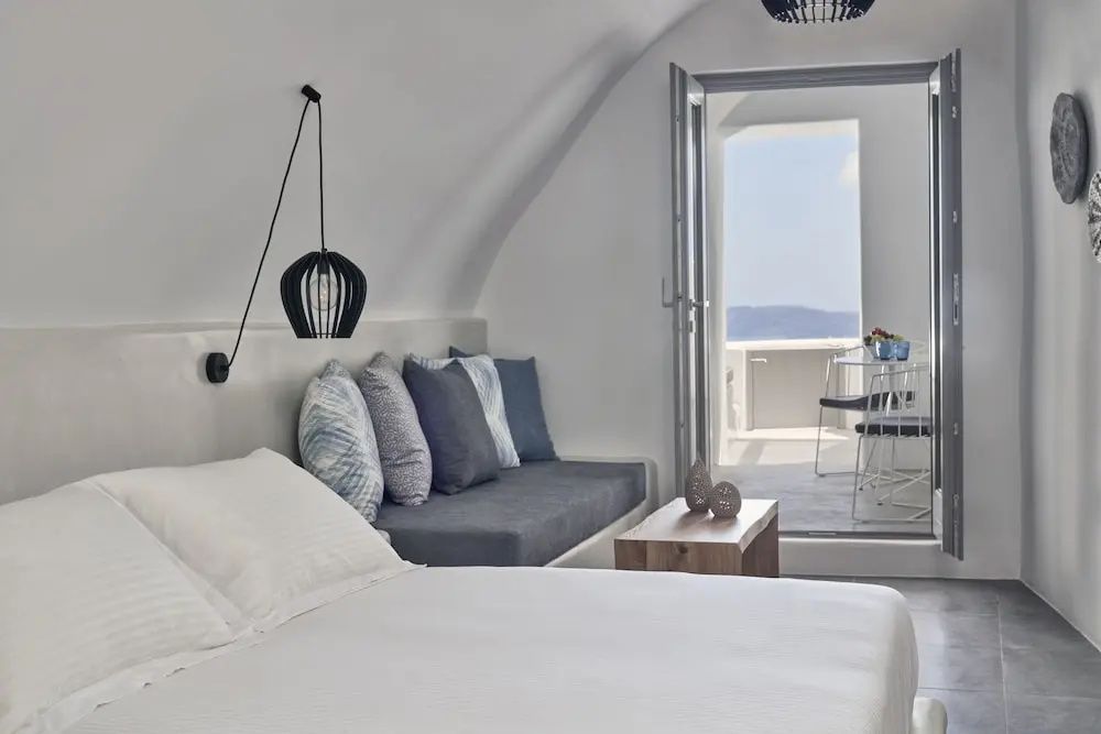 Schlafzimmer mit Doppelbett, Sitzbank und Blick durch die offene Tür nach draußen.