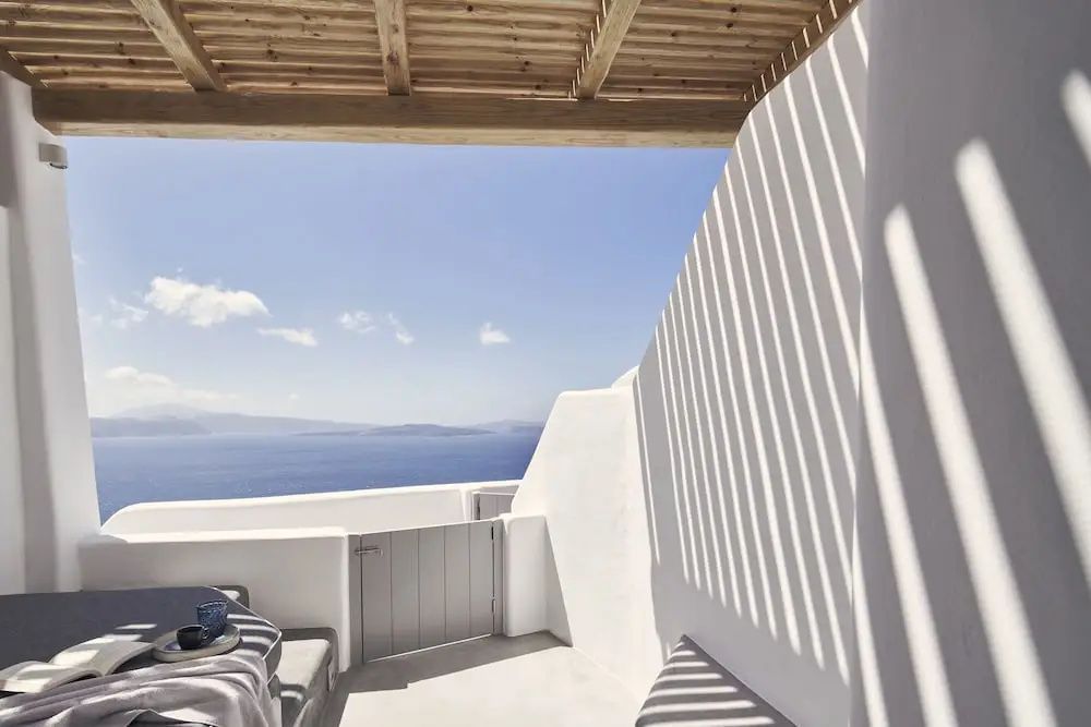 Weiß getünchte Terrasse mit Holzpergola und Blick auf das blaue Meer unter blauem Himmel.