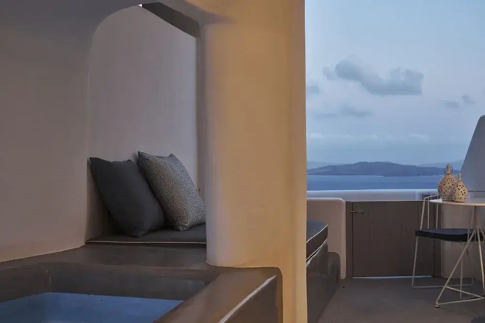 Überdachter Sitzbereich mit grauen Polstern auf einer Terrasse mit Blick auf das Meer.