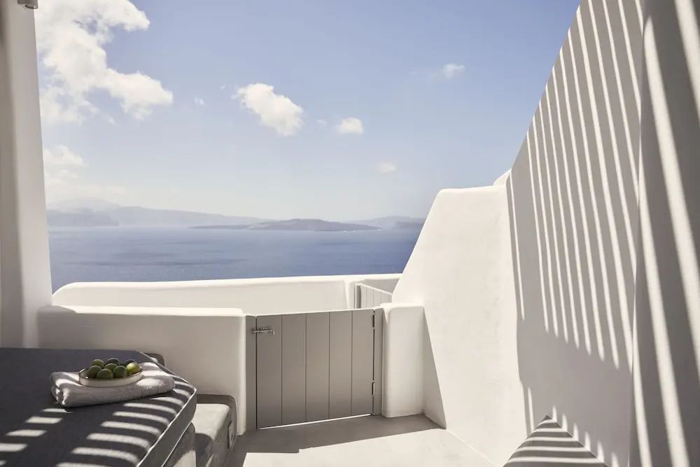 Weiße Terrasse mit Holzpforte und Sitzecke mit Blick auf das blaue Meer.