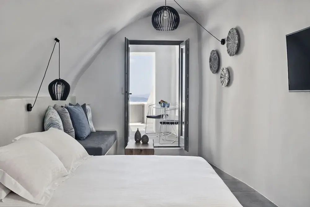 Weißes Höhlenschlafzimmer mit Doppelbett, Sitzecke und offenem Zugang zur Terrasse.
