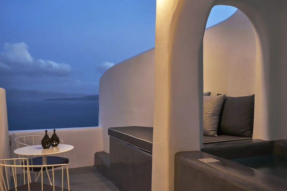 Sitzbereich einer Terrasse am Abend mit dunklen Polstern und Blick auf das dunkle Meer.