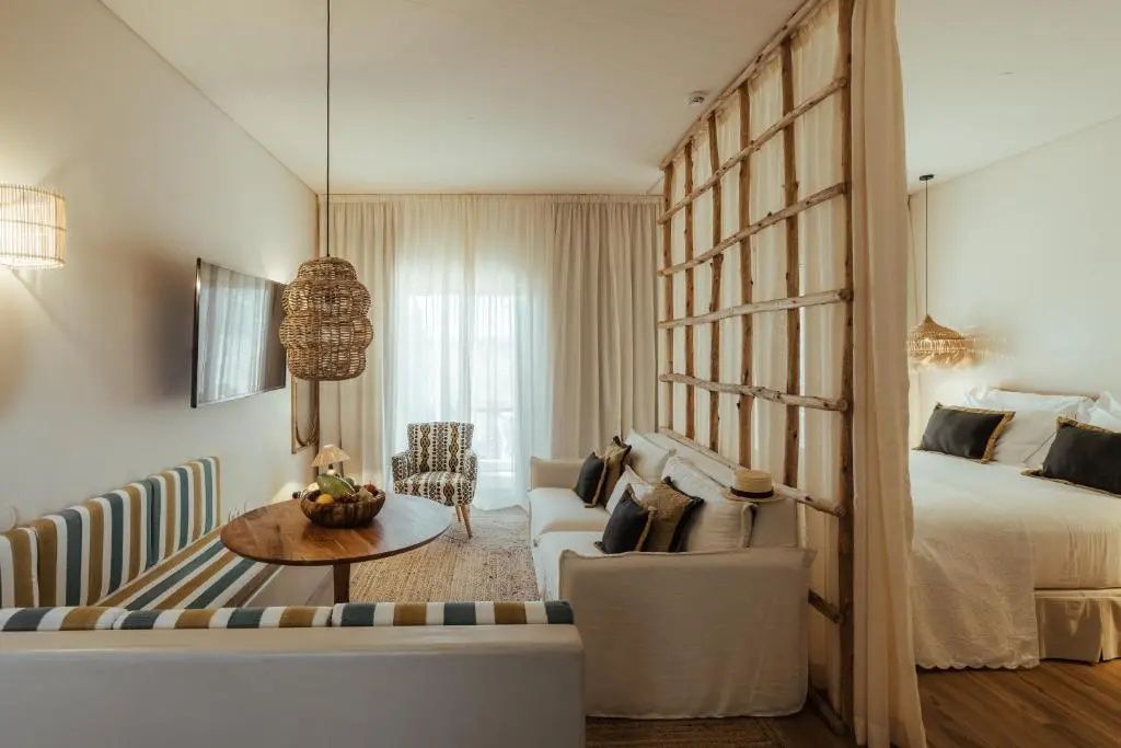 Wohnbereich eines Zimmers mit weißem Sofa, Raumtrenner aus Holz und rundem Esstisch.