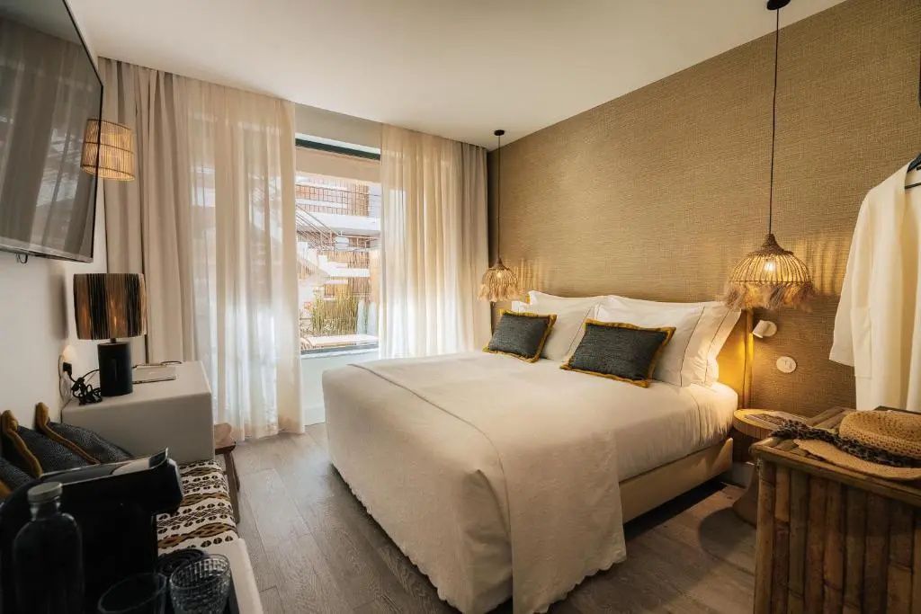 Helles Hotelzimmer mit großem Doppelbett, neutraler Tapete und transparenten Vorhängen.