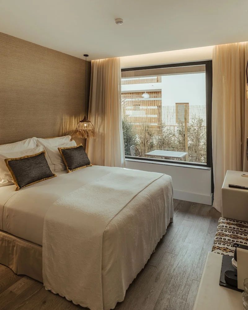 Hell eingerichtetes Hotelzimmer mit Doppelbett und Blick durch ein großes Fenster