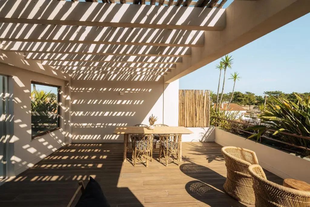 Überdachte Holzterrasse mit Esstisch, Stühlen und Schattenspielen unter einer Pergola.