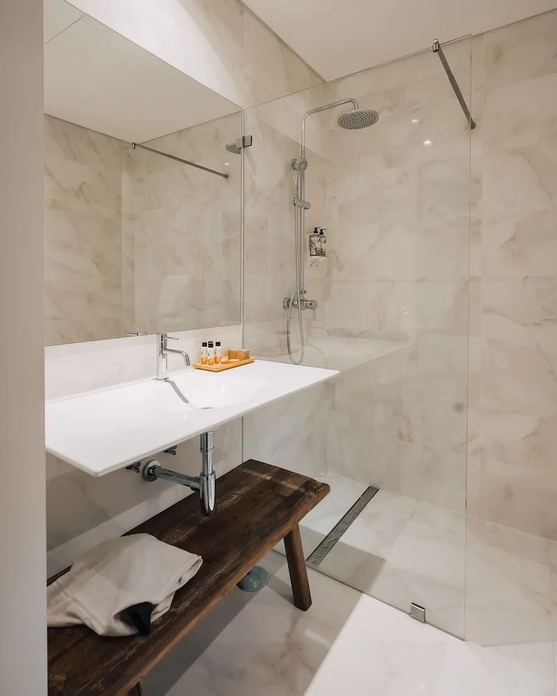 Modernes Badezimmer mit weißem Waschbecken, großer Regendusche und einer Holzbank.