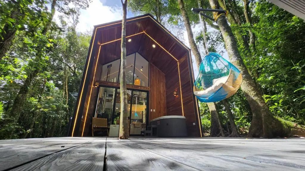 Moderne Holzhütte im Wald mit beleuchteter Fassade, Terrasse und Whirlpool.