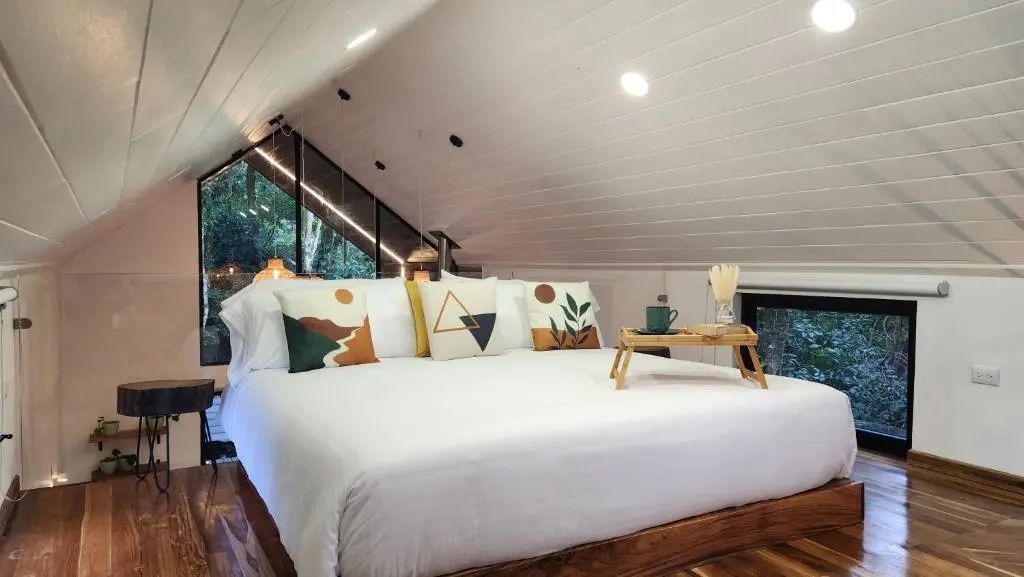 Großes Doppelbett mit Kissen unter einer weißen Holzdecke und ein Tablett mit Tasse.