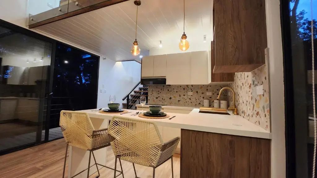 Offene Küche mit Frühstückstheke, zwei Stühlen, Terrazzo-Rückwand und Hängelampen.