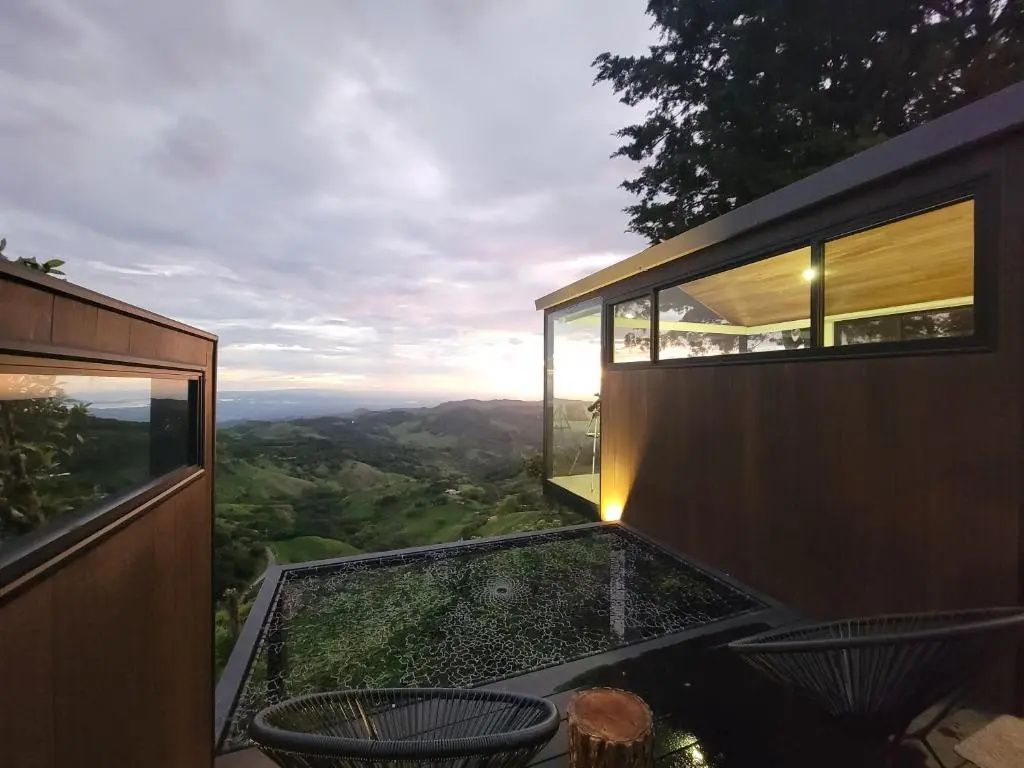 Moderne Hütte mit Terrasse und Ausblick auf hügelige Landschaft im Abendlicht.