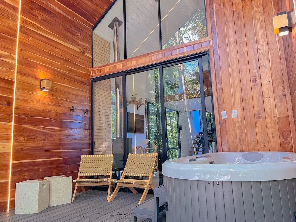 Überdachte Holzterrasse mit Whirlpool, Stühlen und hoher Fensterfront.