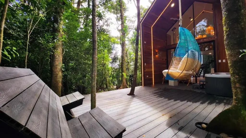 Großzügige Holzterrasse mit Hängesessel mitten in einem dichten Wald.