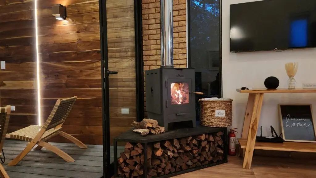 Brennender Kaminofen aus Gusseisen mit Holzvorrat darunter auf dunklen Fliesen.