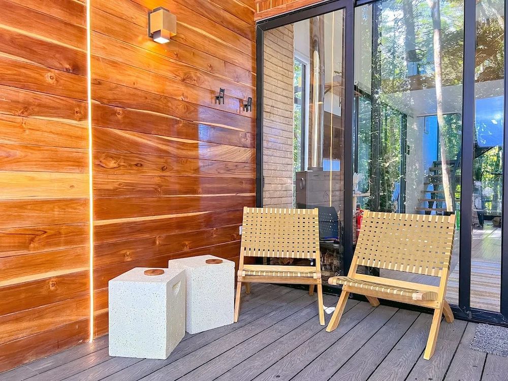 Holzterrasse mit zwei Flechtsesseln und kleinen Beistelltischen vor einer Glasfront.