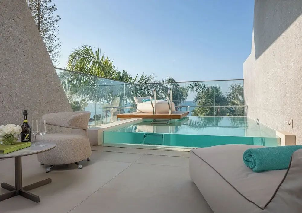 Terrasse mit Sitzgelegenheiten, kleine Poolanlage und Weitblick auf Palmen und Meer.