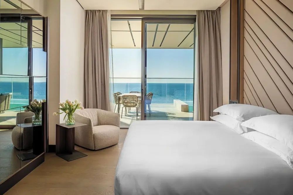 Schlafzimmer mit großem Doppelbett und Fensterfront mit Blick auf das Meer.