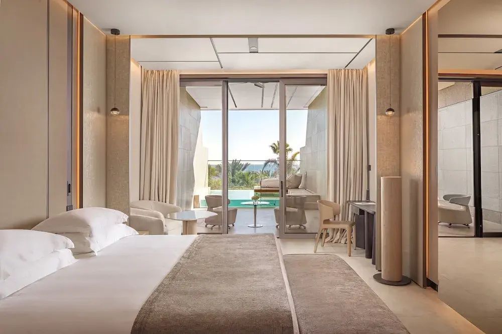 Helles Hotelzimmer mit Doppelbett und Zugang zur Terrasse mit Pool und Meerblick.