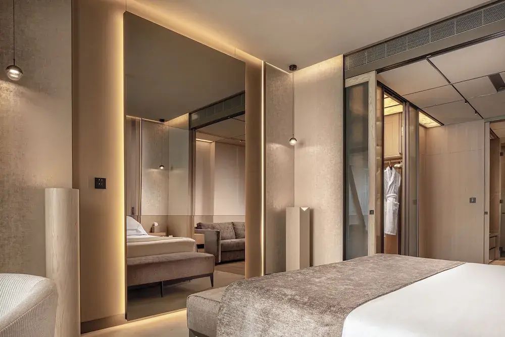 Schlafzimmer mit großem Spiegel, indirekter Beleuchtung und Blick in die Ankleide.