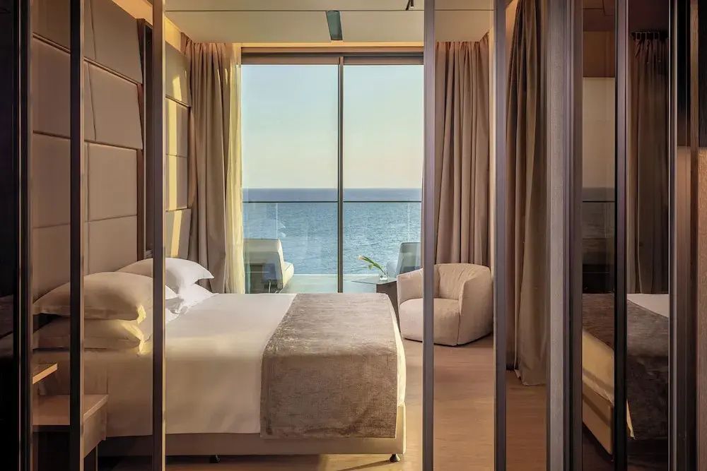Schlafzimmer mit Doppelbett und Blick durch die Glasfront auf das Meer.