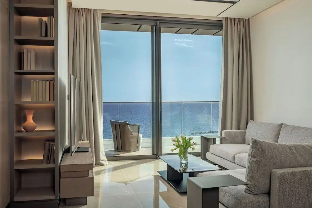 Wohnzimmer mit hellem Sofa und Schiebetür zum Balkon mit Meeresblick.