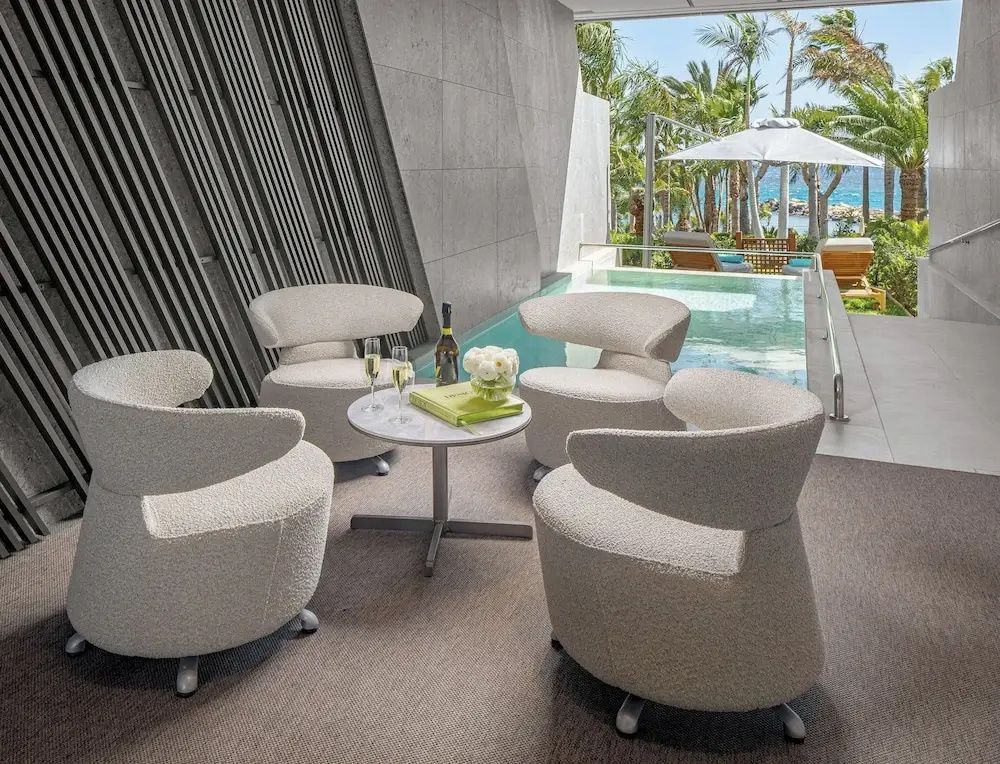 Überdachte Terrasse mit gemütlichen Sesseln und Blick auf einen privaten Pool und Palmen.