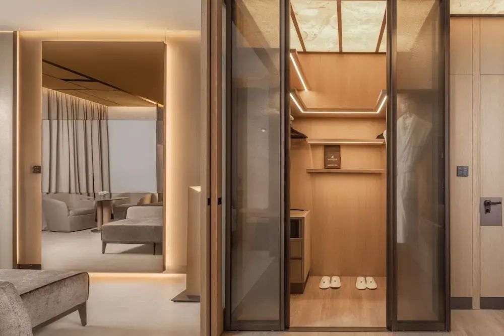 Beleuchteter begehbarer Kleiderschrank aus Holz mit Schiebetüren aus Glas in einer Suite.