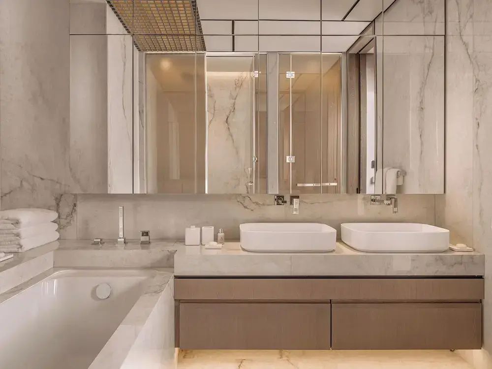 Badezimmer mit zwei Aufsatzwaschbecken, verspiegelten Schränken und Marmorwand.