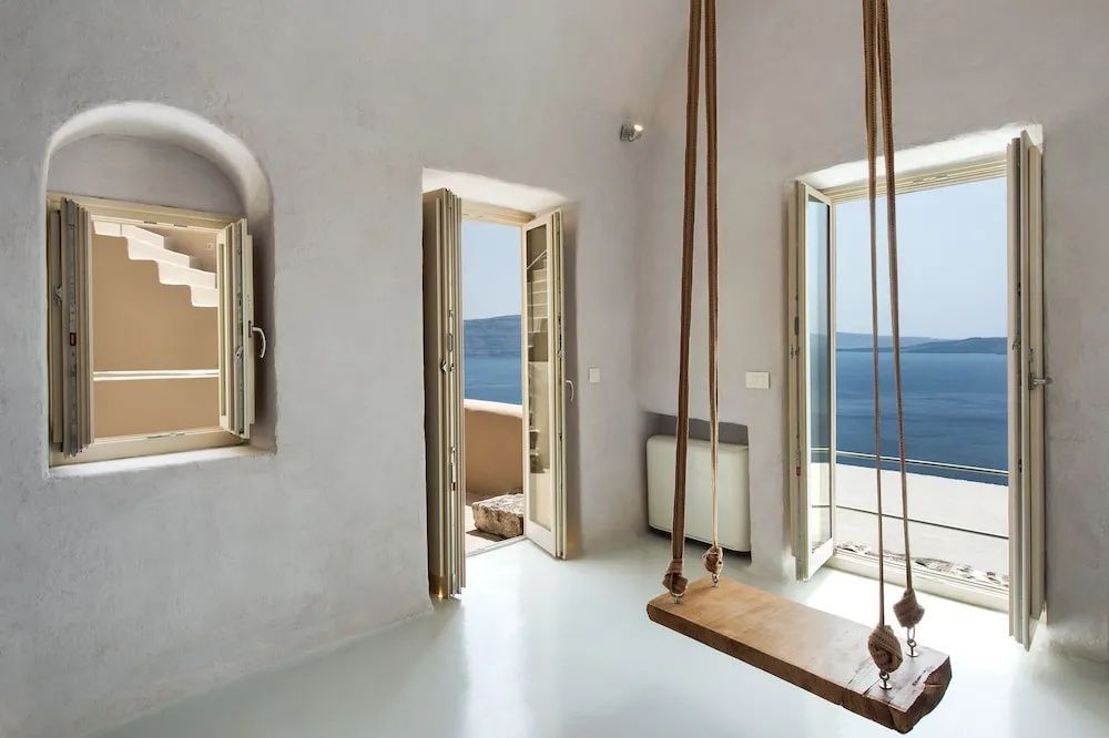 Heller Innenraum mit Holzschaukel und geöffneten Türen mit Blick auf das Meer.