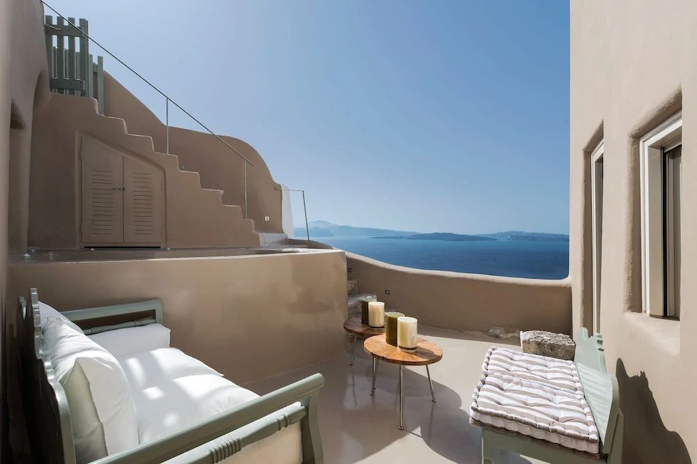 Sonnenterrasse mit Sitzbänken, kleinen Tischen und freiem Blick auf das Ägäische Meer.