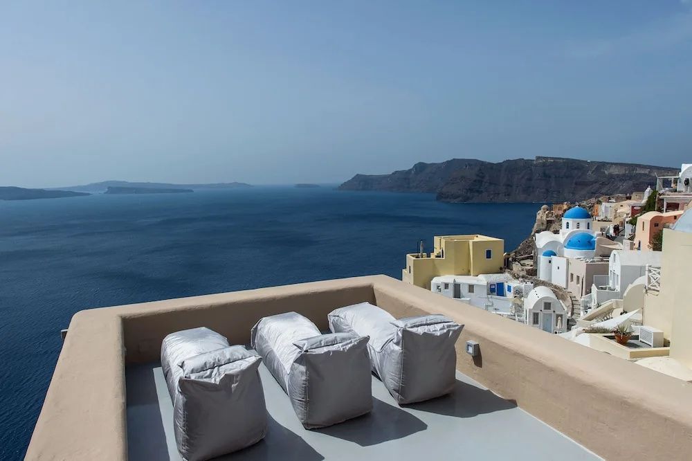 Dachterrasse mit drei weichen Liegestühlen und Aussicht auf das Meer und Felsformationen.