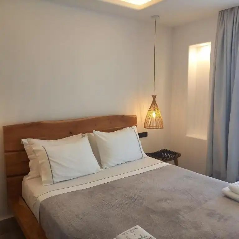 Doppelbett mit Holzkopfteil, weißer Bettwäsche und einer hängenden Flechtlampe.