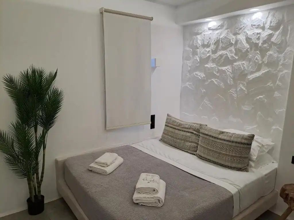 Doppelbett mit grauer Tagesdecke vor einer weißen Steinwand im Hotelzimmer.