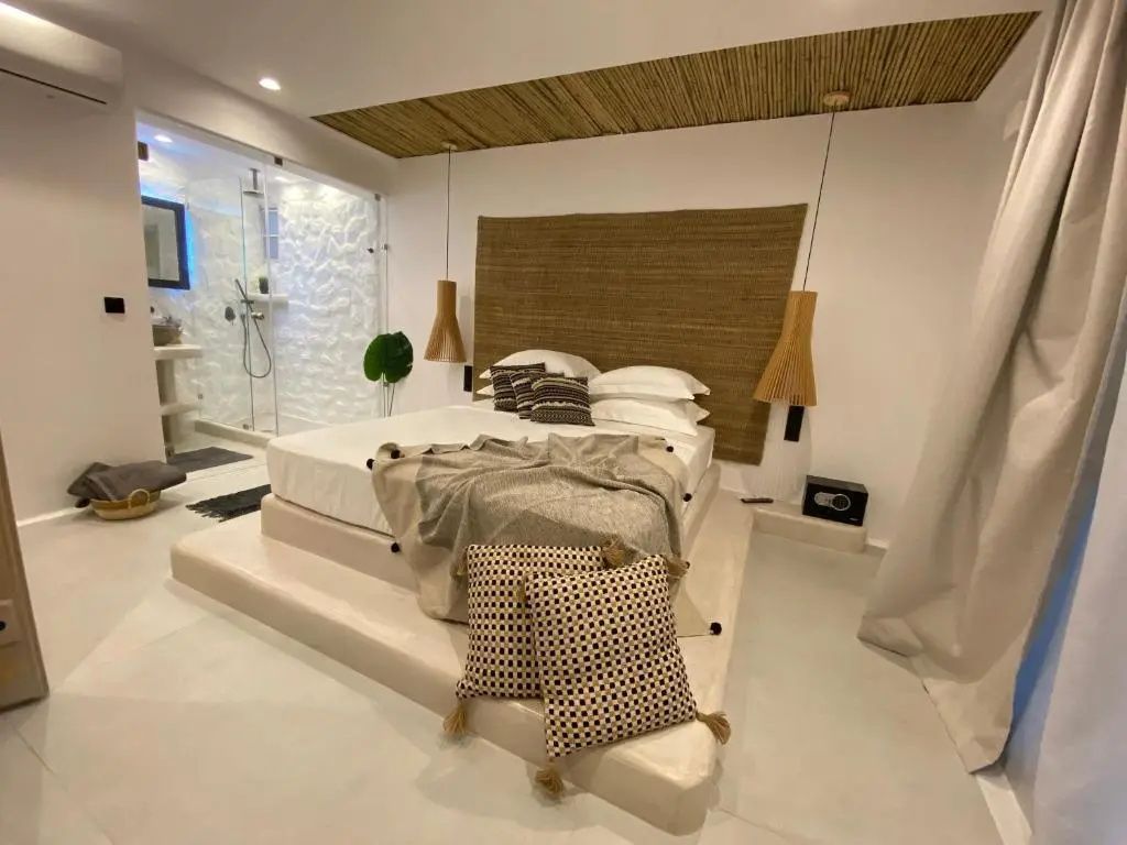 Doppelbett auf erhöhtem Sockel mit dekorativen Kissen und Blick ins angrenzende Badezimmer.