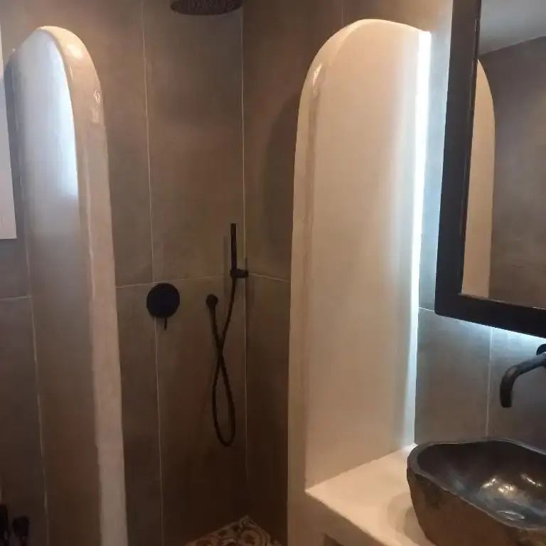 Badezimmer mit offenem Duschbereich, dunklen Fliesen und einem Steinwaschbecken.