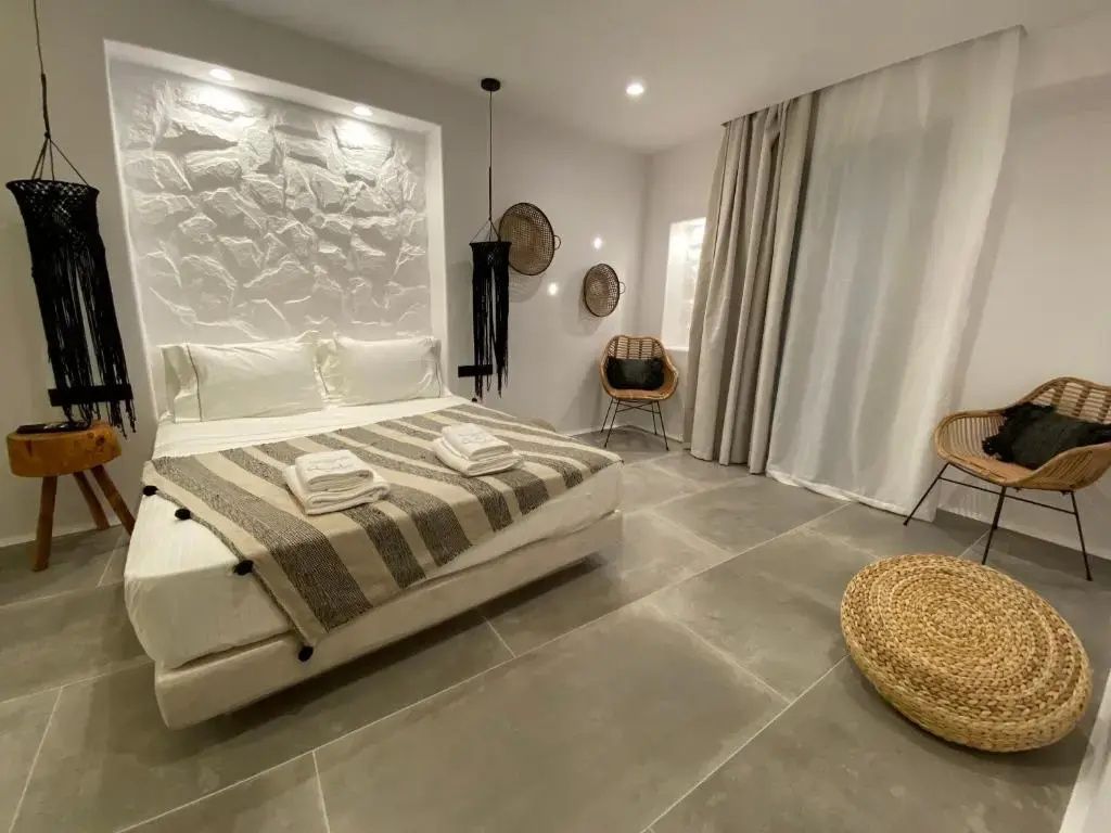 Schlafzimmer mit hellem Bett, gestreifter Decke, Wandnische in Steinoptik und Sessel.