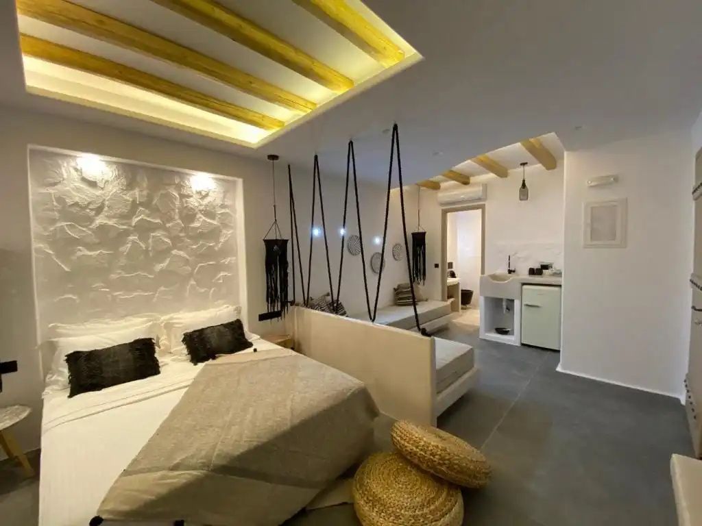 Offener Schlafbereich mit Holzdecke, Rattanpuffs und kleiner Küchenzeile im Hintergrund.