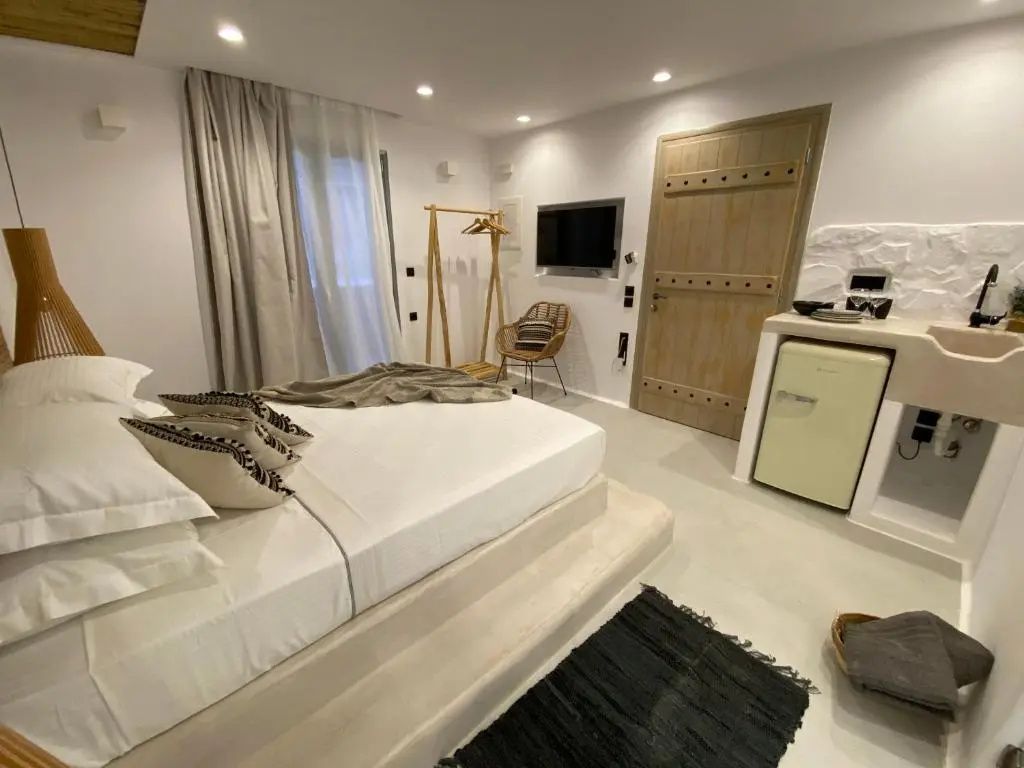 Schlafbereich mit Fernseher an der Wand, kleine Minibar und Sitzgelegenheit neben der Tür.