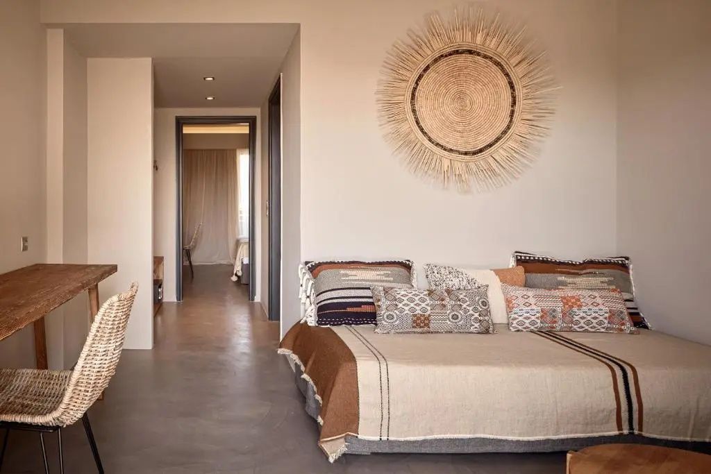 Wohnbereich eines Hotelzimmers mit einem Bettsofa, Wanddekoration aus Stroh und Durchgang zum Schlafzimmer.