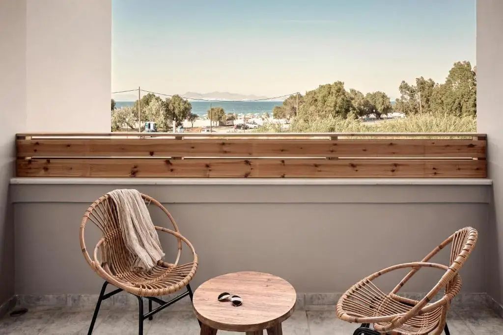 Balkon mit zwei Rattanstühlen und einem Holzbeistelltisch mit Blick auf Bäume und das Meer.