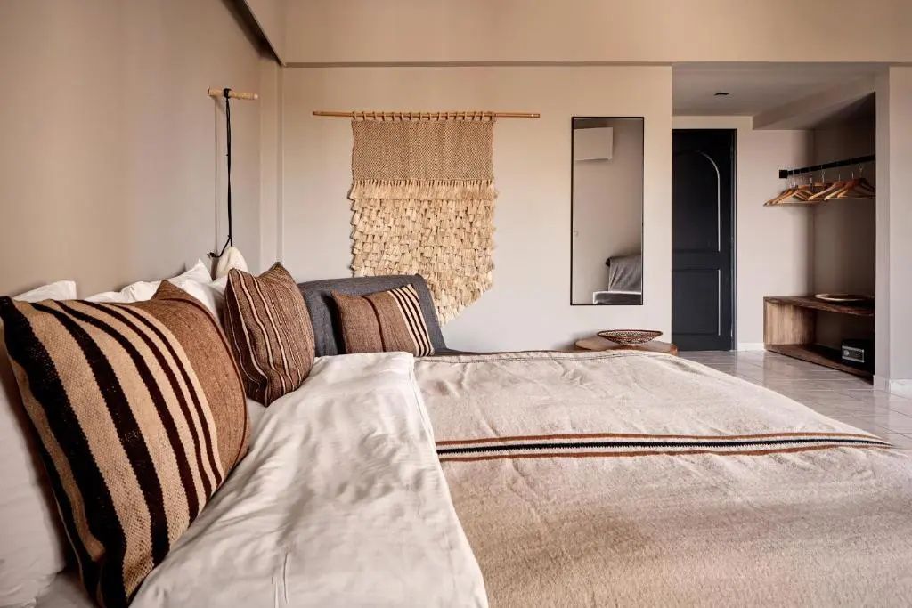 Hell gestaltetes Zimmer mit Doppelbett, gestreiften Kissen und einem Wandteppich