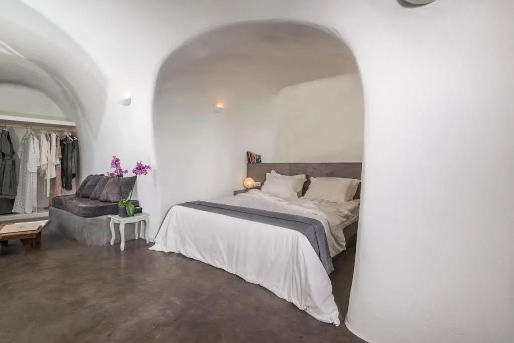 Doppelbett in einer weiß getünchten Höhlensuite mit dunklem Steinboden und einer Sitzecke.