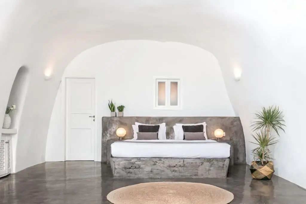 Weißes Höhlenzimmer mit einem Doppelbett, zwei Lampen und dunklem Boden.
