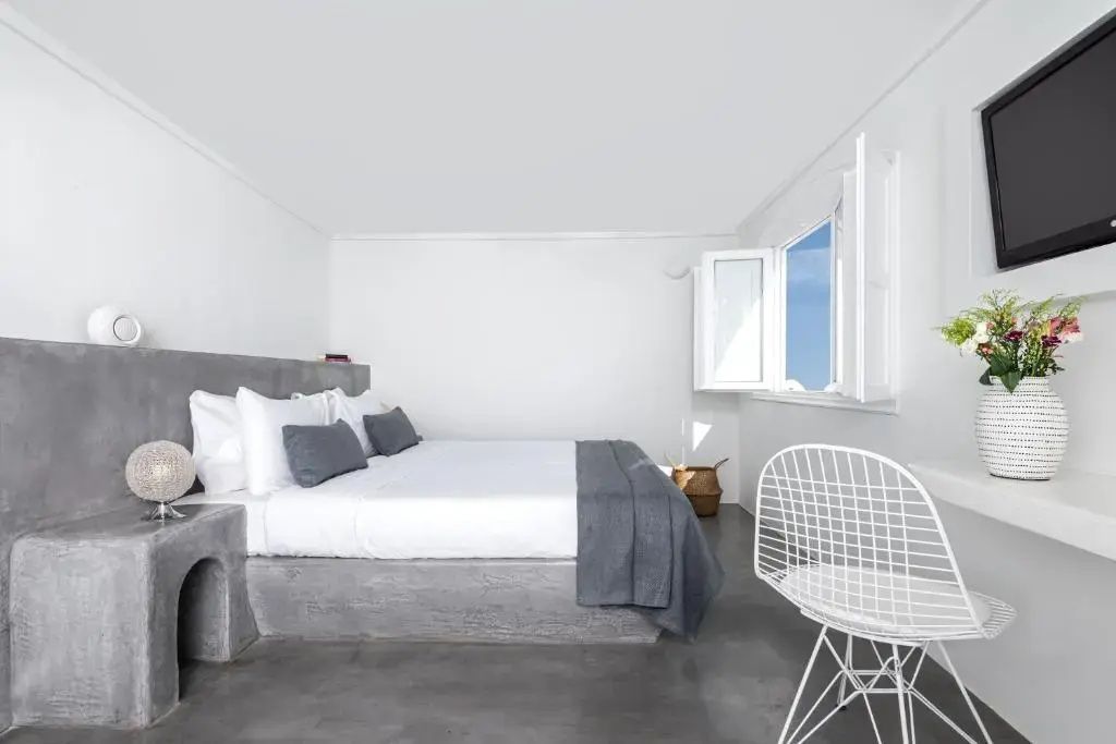 Schlafzimmer in Weiß und Grau mit Doppelbett, weißem Stuhl und geöffnetem Fenster.