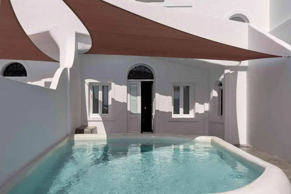 Ein kleiner Pool auf einer weißen Terrasse unter einem braunen Sonnensegel.