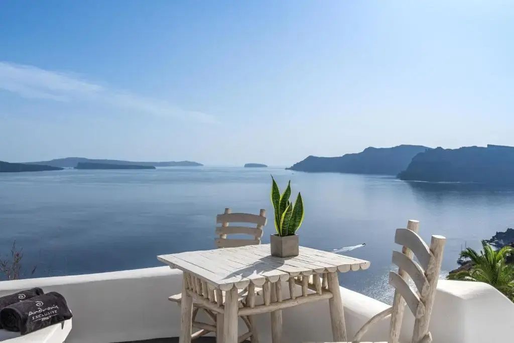 Sitzplatz auf einer Terrasse mit Holztisch und Blick auf das blaue Meer und Inseln.