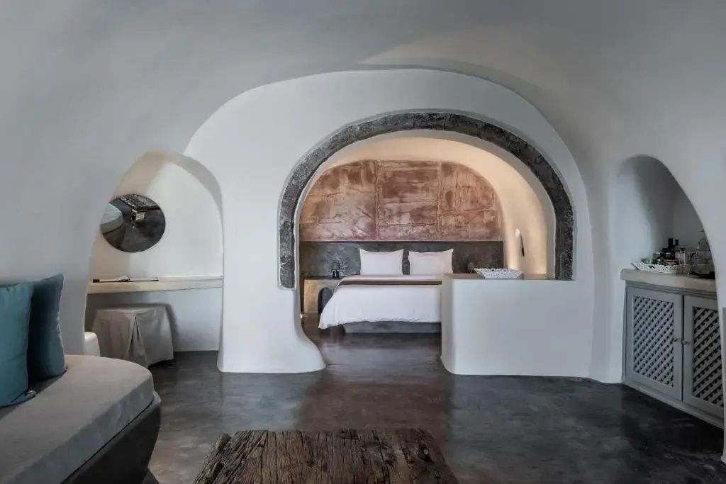 Weiß getünchte Höhlensuite mit dunklem Steinbogen vor dem Doppelbett im Hintergrund.